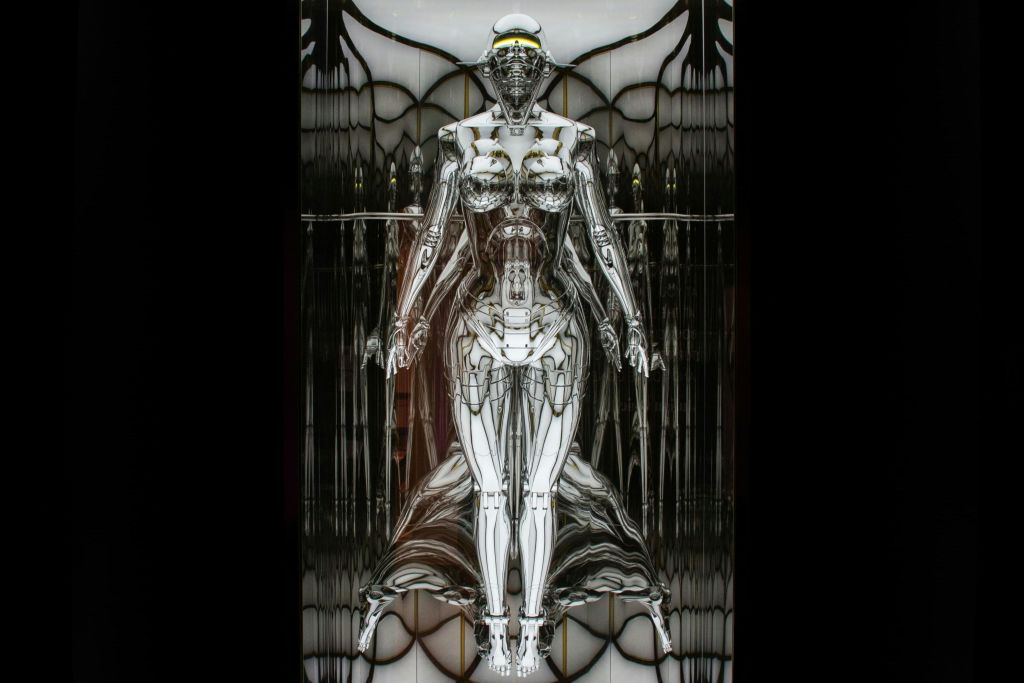 금속 반사 표면이 있는 미래형 휴머노이드 로봇은 대칭적이고 추상적인 배경에 서 있습니다.