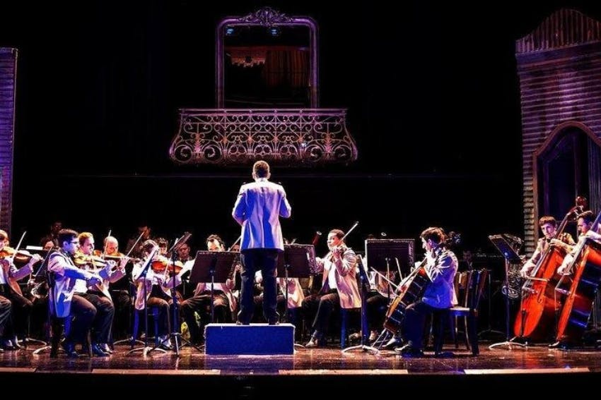 화려한 발코니 난간 아래에서 뒤에서 바라본 지휘자와 함께 무대에서 공연하는 오케스트라.