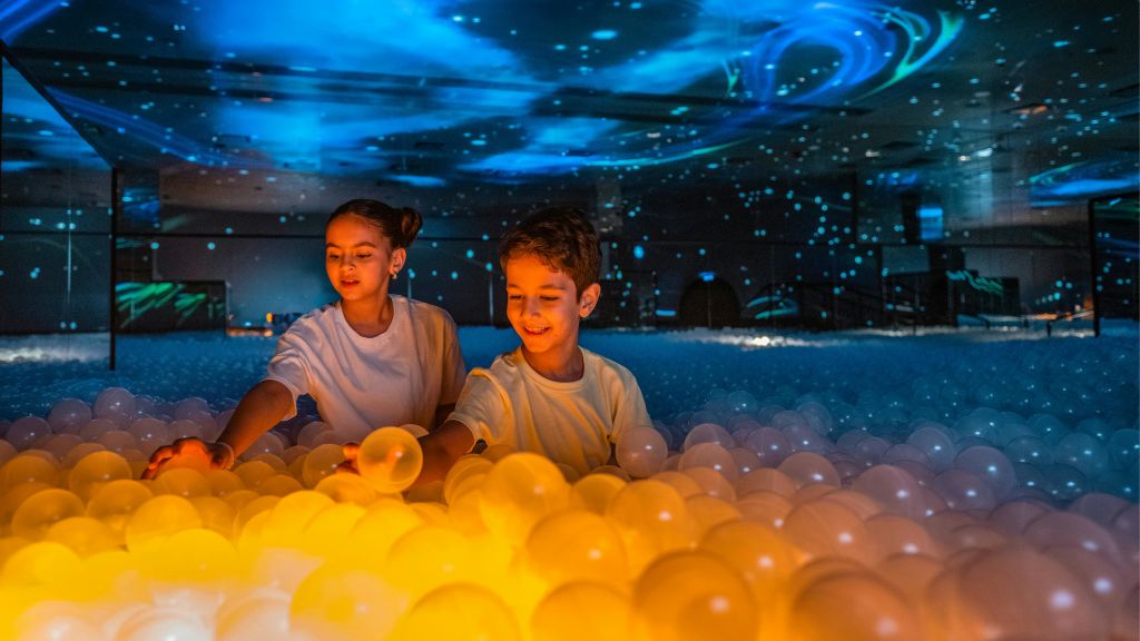 파란색과 주황색 조명이 있는 어두운 방에서 두 아이가 조명 공을 가지고 놀고 있습니다.