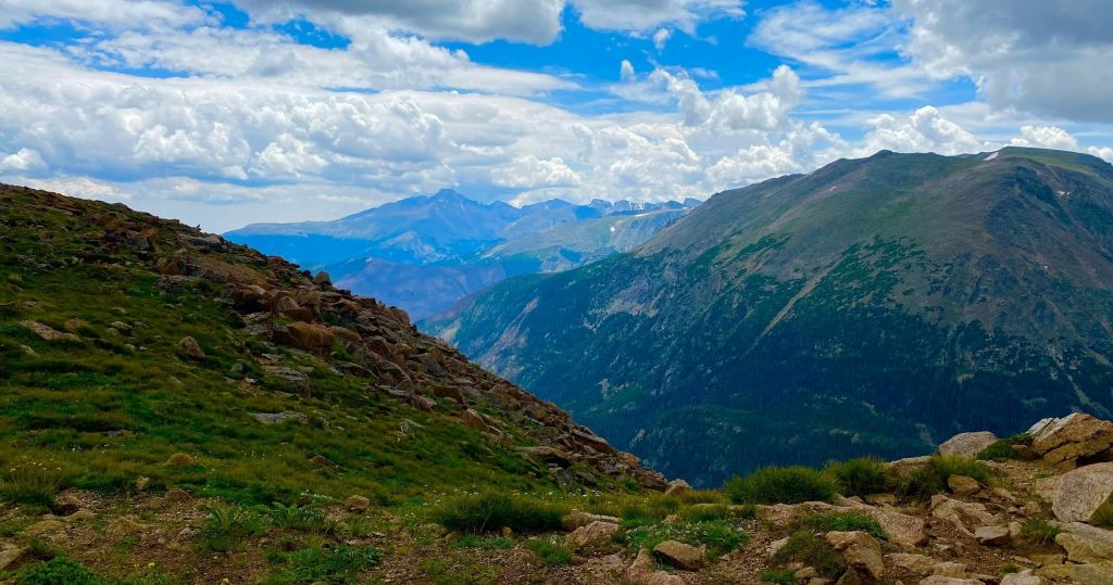 부분적으로 흐린 푸른 하늘 아래 바위 지형, 푸른 비탈, 먼 봉우리가 있는 산 풍경.