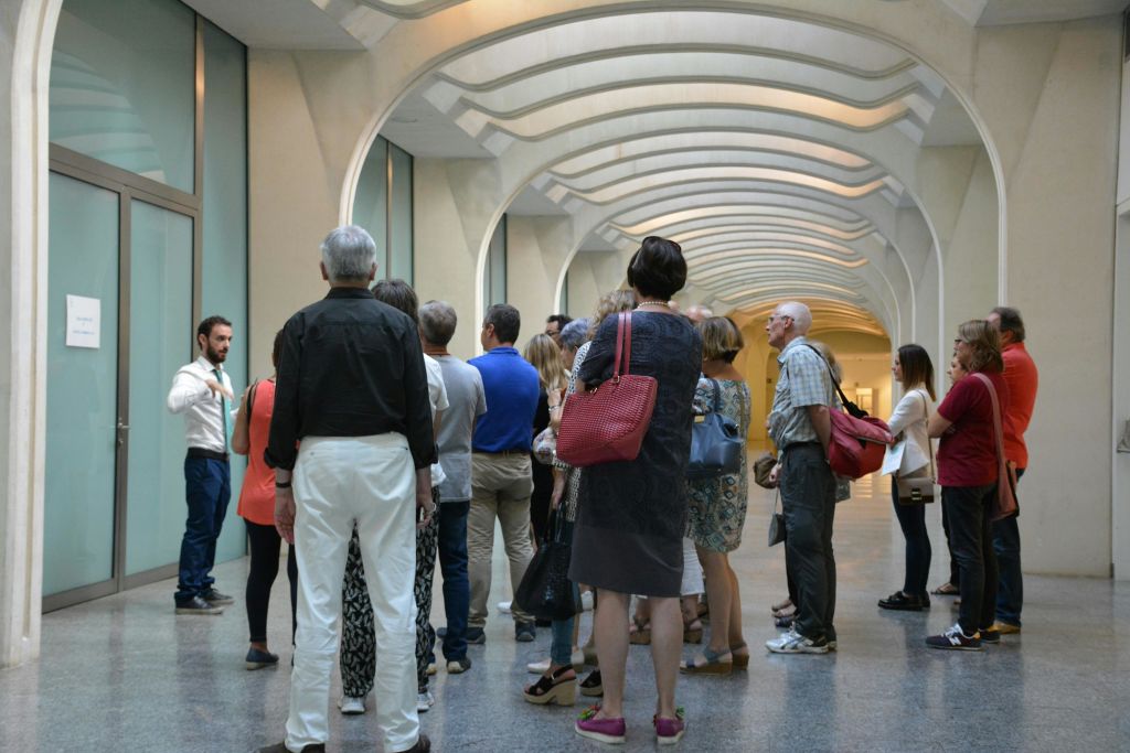 가이드가 곡선형 천장 아치와 유리문이 있는 현대적인 복도에 있는 사람들을 소개합니다.
