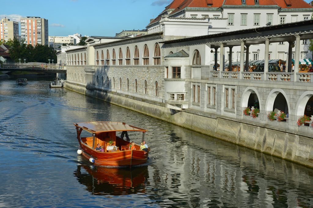 아치형 창문과 야외 테라스가 있는 오래된 석조 건물 옆 운하에 캐노피가 달린 작은 나무 보트가 떠 있습니다.