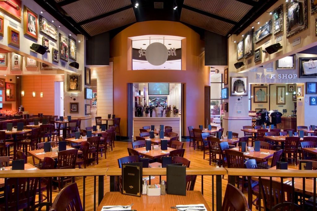 나무 테이블과 의자, 우아한 인테리어, 크림색과 주황색 벽에 그림 액자가 있는 넓고 현대적인 레스토랑입니다.