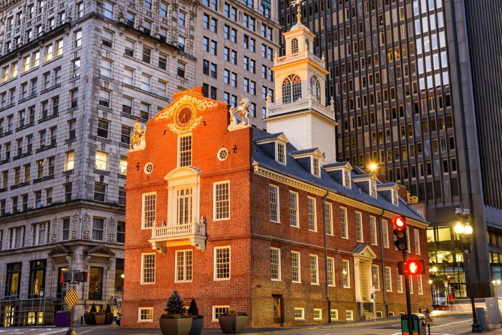 하얀 테두리와 시계탑이 있는 유서 깊은 붉은 벽돌 건물로 현대적인 고층 건물로 둘러싸여 있습니다.