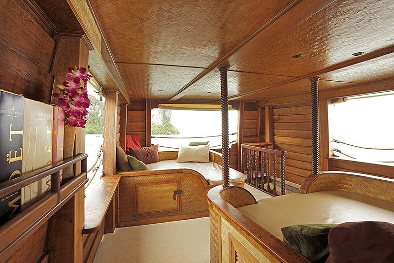 쿠션이 있는 좌석, 베개, 꽃, 창문이 있는 아늑한 나무 보트 인테리어는 야외 물과 섬의 풍경을 보여줍니다.