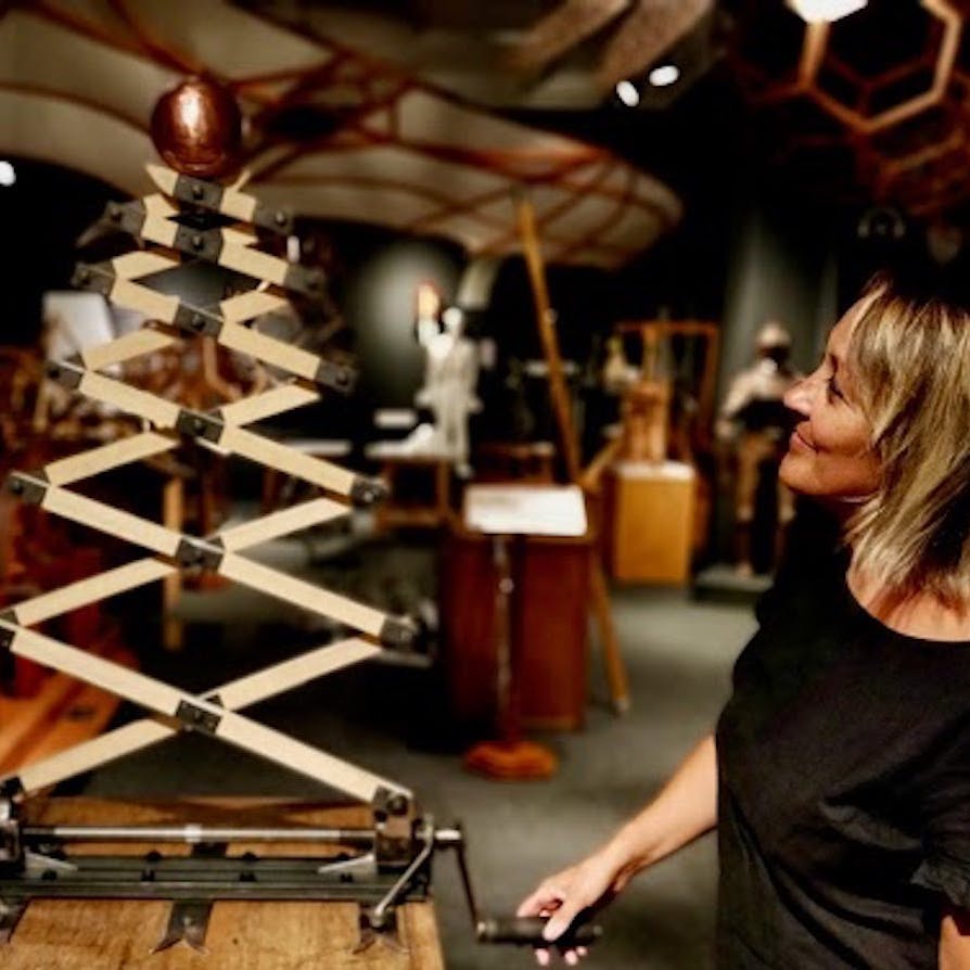 한 여성이 박물관 내부나 전시 공간에서 기계식 목조 건축물을 보며 미소를 짓고 있습니다.