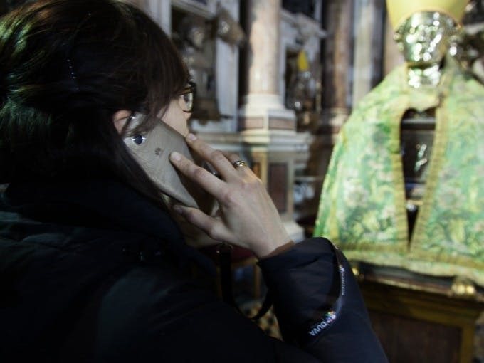 휴대폰을 귀에 대고 건물 내부에 기둥이 있는 녹색 천으로 장식된 화려한 동상을 마주하고 있는 사람.