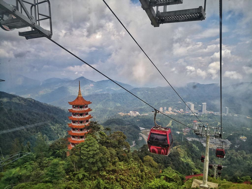 울창한 푸른 언덕을 가로지르는 케이블카와 붉은 탑을 배경으로 한 도시 풍경이 펼쳐집니다.