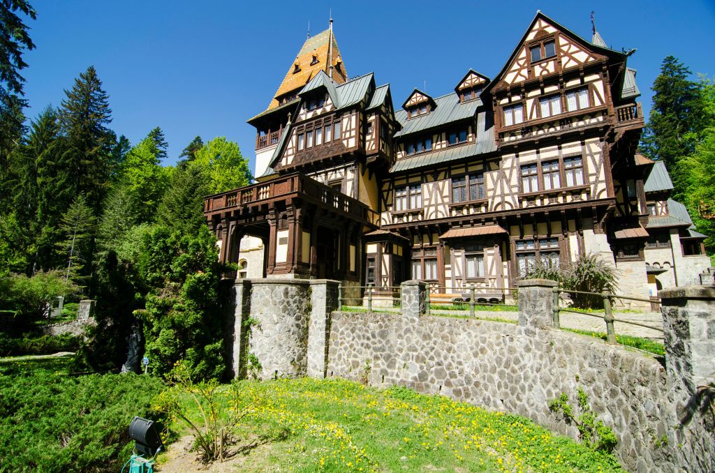 맑고 화창한 날에 울창한 녹지로 둘러싸인 발코니가 있는 크고 화려한 목재와 석조 건물입니다.