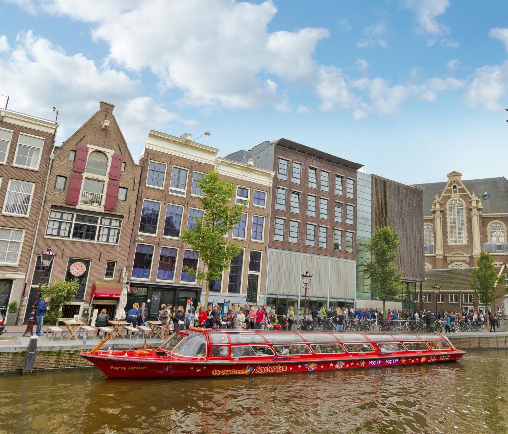 전통 건물과 현대적인 건물이 줄지어 있는 붉은 운하 보트가 워터프론트를 따라 걷고 있습니다.