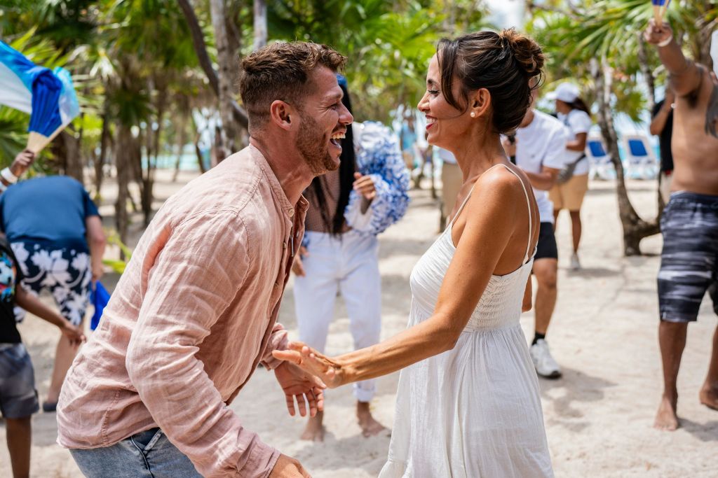 한 남자와 한 여자가 사람들과 야자수를 배경으로 야외에서 웃고 손을 잡습니다.