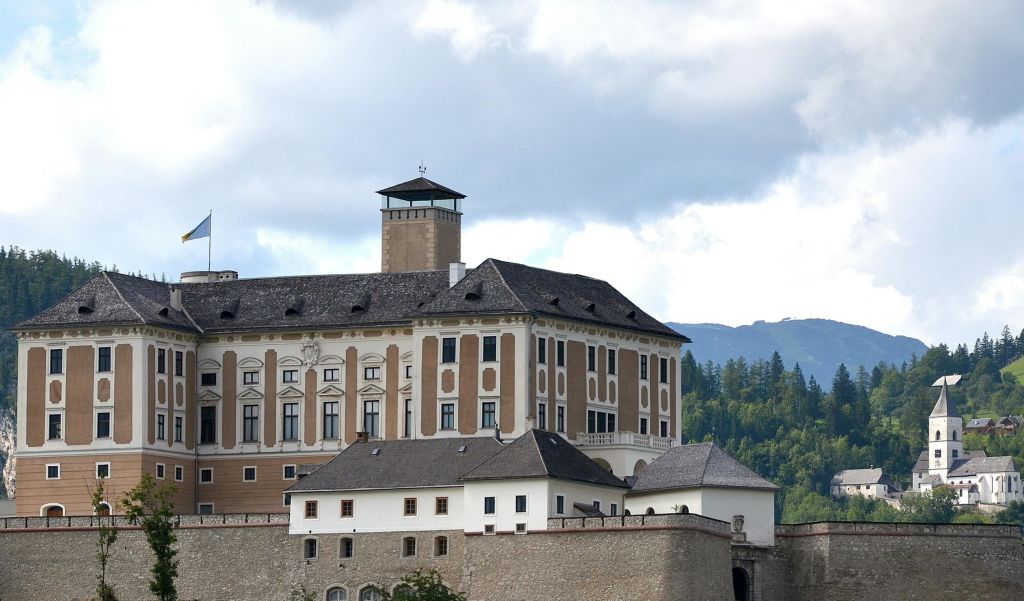 나무와 흐린 하늘을 배경으로 높은 창문과 탑이 있는 역사적인 복층 건물입니다.