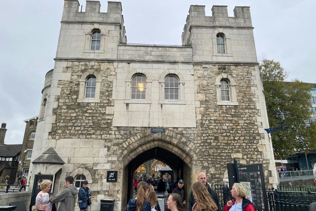 바깥에 사람들이 모여 있는 석조 아치형 통로 입구. 표지판에는 "부두로" 라고 쓰여 있습니다. 나무와 상점이 배경으로 보입니다.