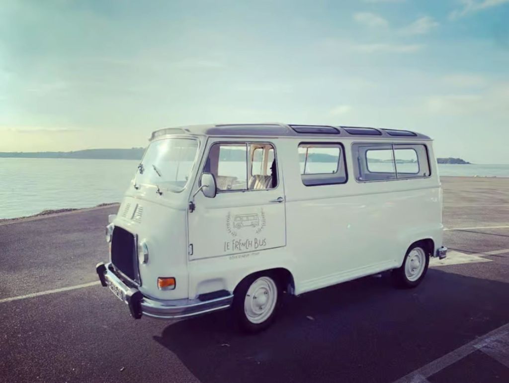 "Le French Bus" 가 적힌 바닷가에 주차된 흰색 빈티지 밴입니다.