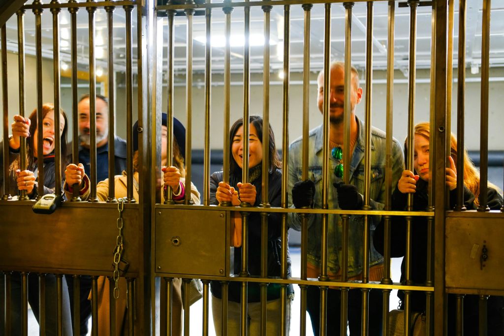 한 무리의 사람들이 금속 문 뒤에 서서 미소를 지으며 바를 잡고 있습니다. 배경은 실내 환경을 보여줍니다.