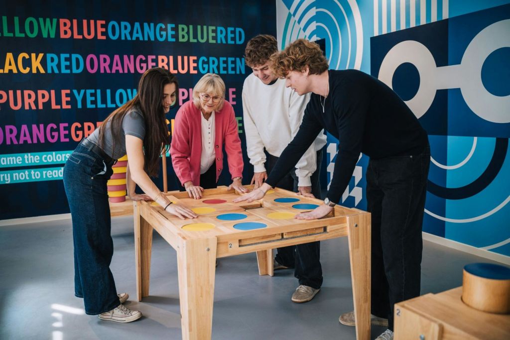 네 명의 그룹이 활기찬 텍스트와 패턴이 있는 벽으로 둘러싸인 다채로운 테이블 게임과 상호 작용합니다.