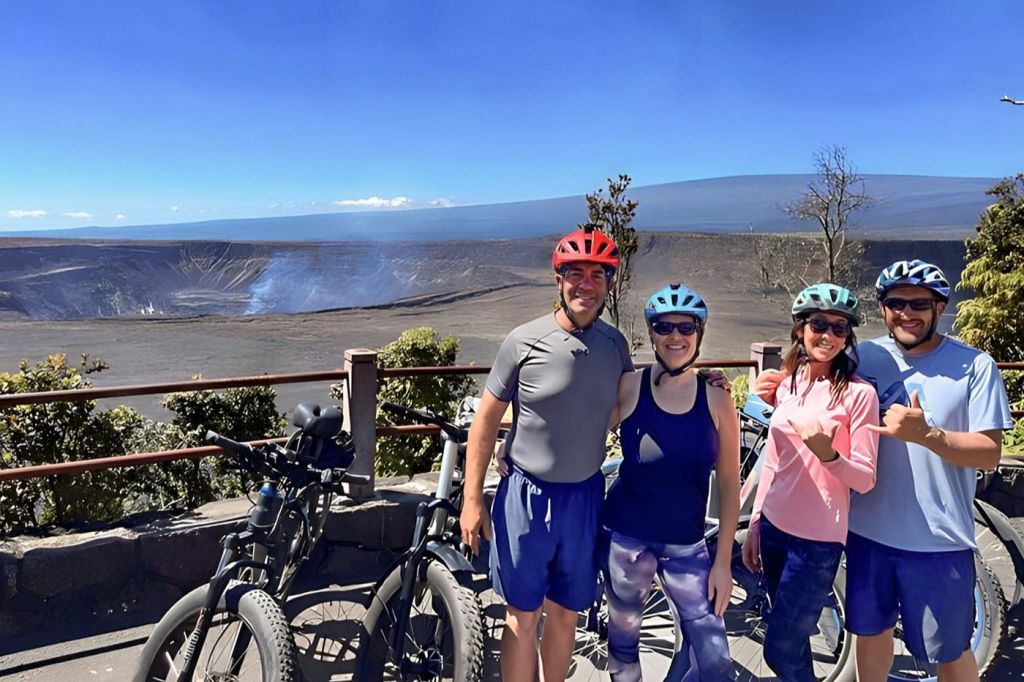 자전거 장비와 헬멧을 쓴 네 명이 광활하고 황량한 풍경과 푸른 하늘 앞에서 자전거를 들고 포즈를 취하고 있습니다.