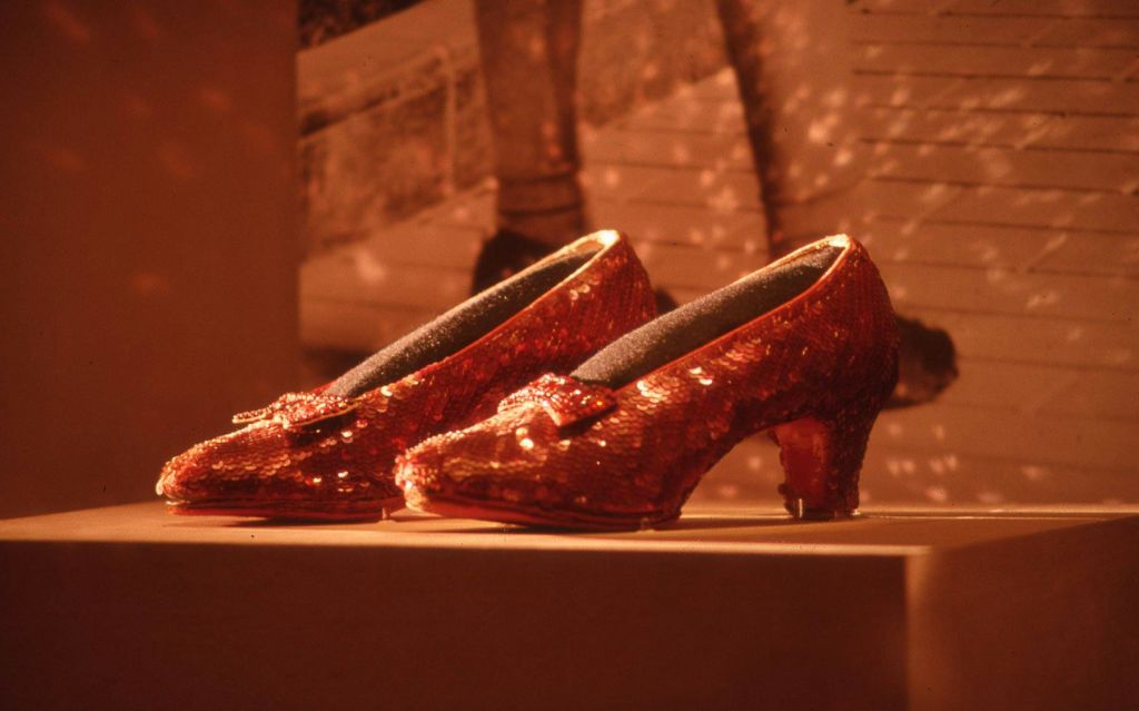 흑백 이미지가 있는 흐릿한 배경에 활이 있는 스팽글 레드 하이힐 슈즈.