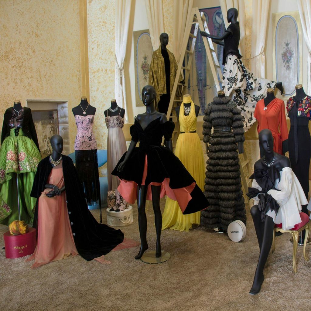 카펫 바닥에 가운과 정장 등 다양한 정교한 드레스를 입은 여러 마네킹이 놓인 객실입니다.