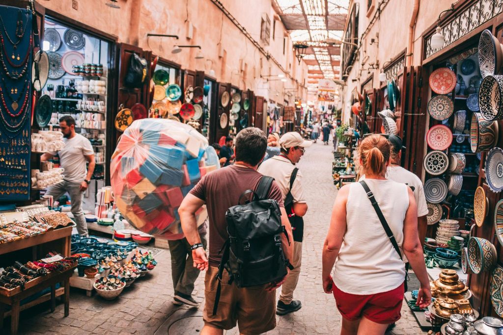 양쪽에 도자기와 다채로운 물품이 진열된 상점들이 즐비한 바쁜 시장 거리를 걷는 사람들.