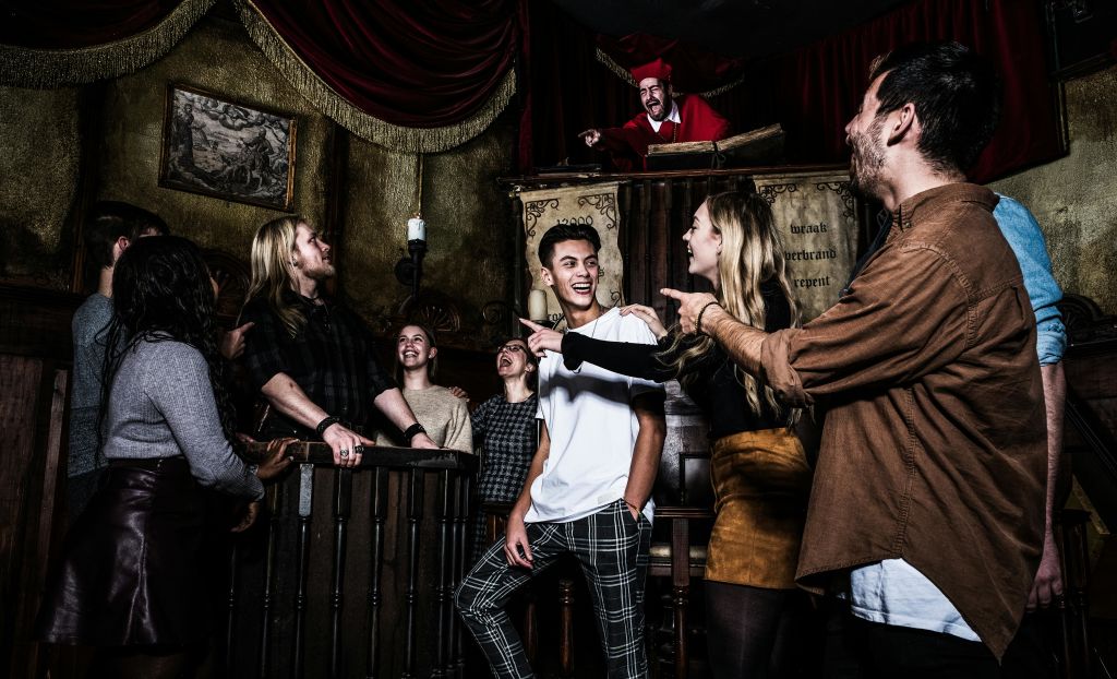 한 무리의 사람들이 화려한 방에서 중세 판사나 관료가 단상에서 가리키는 옷을 입은 채 웃고 있습니다.