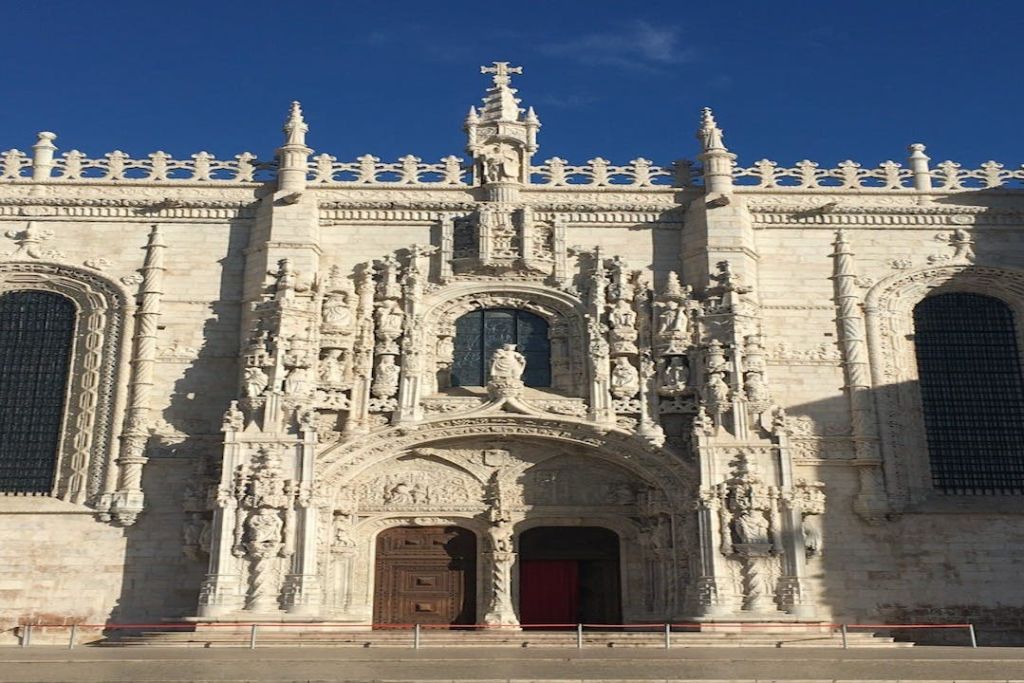 청명한 푸른 하늘을 배경으로 정교한 조각품과 조각상, 커다란 나무 문이 있는 역사적인 건물의 화려한 석조 외관.