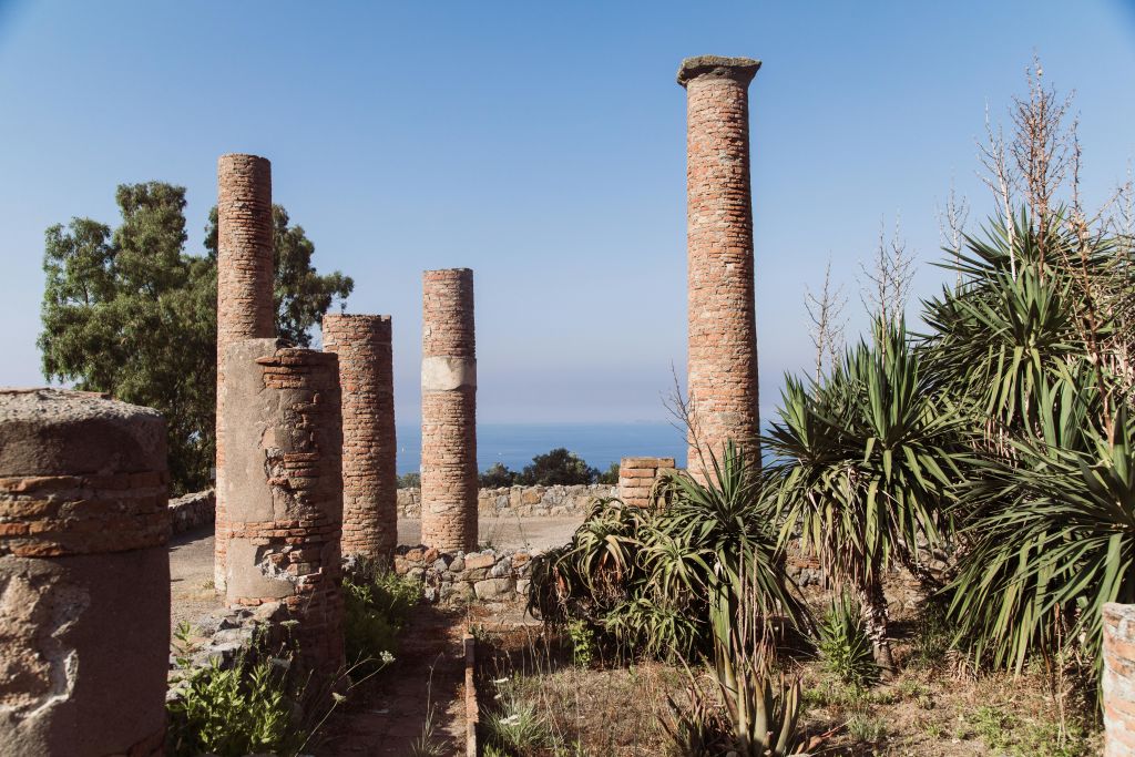 고대의 벽돌 기둥은 바다와 맑고 푸른 하늘을 배경으로 자라난 식물들 사이에 서 있습니다.
