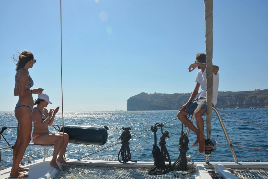 맑고 푸른 하늘 아래 보트에서 휴식을 취하는 두 사람, 멀리 언덕이 많은 해안선과 주변의 잔잔한 바다.