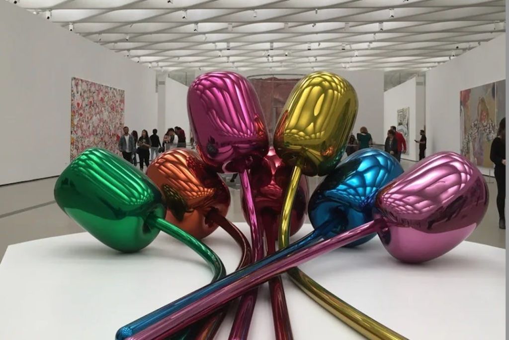 현대 미술관에 있는 다채로운 금속 튤립 조각품으로, 사람들이 다양한 예술 작품을 배경으로 감상합니다.