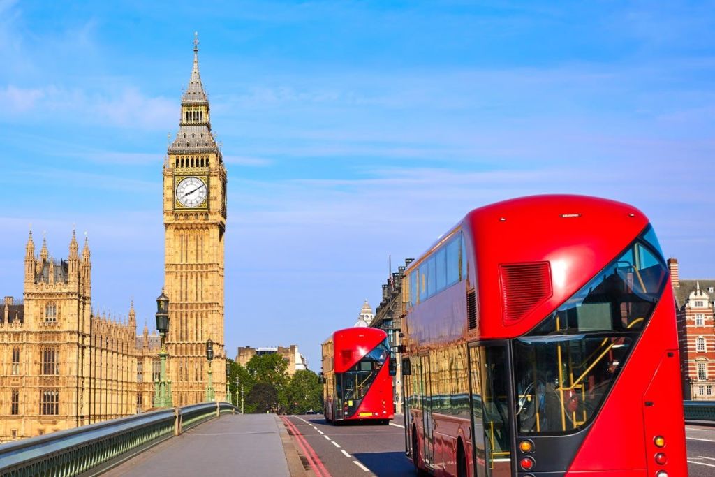 맑고 푸른 하늘 아래 빅벤 시계탑을 배경으로 다리에 빨간색 2층 버스가 있습니다.