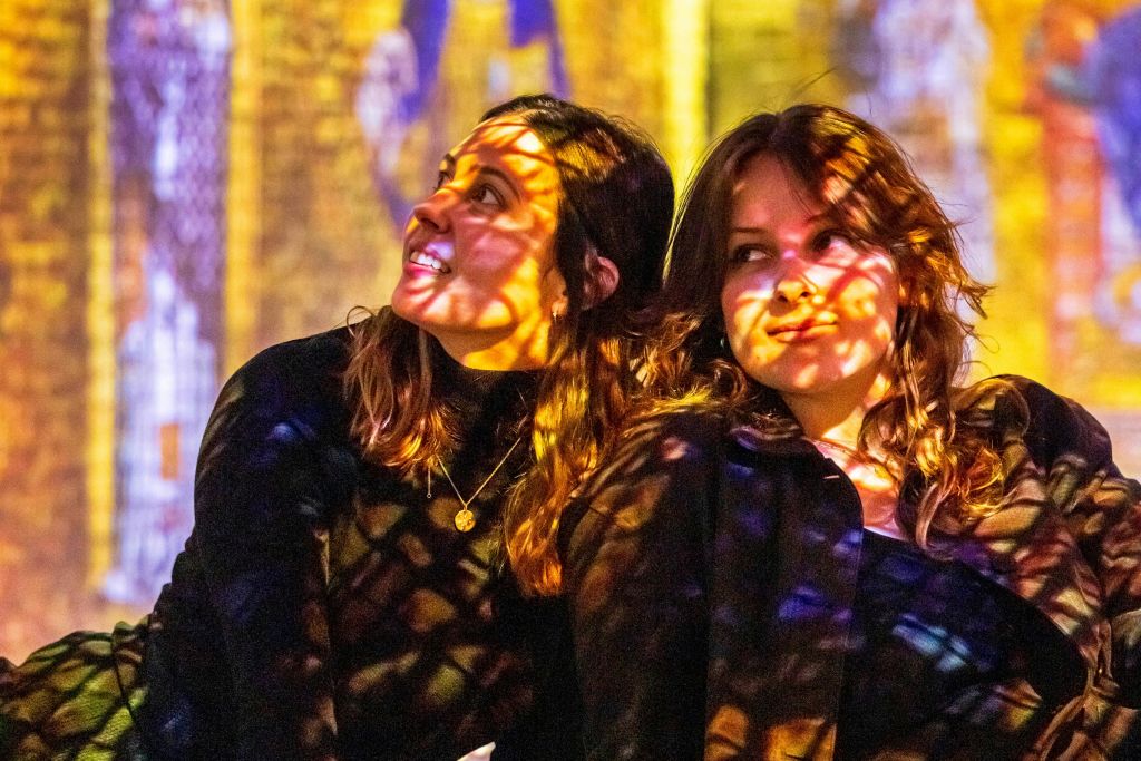 화려한 빛의 무늬를 가진 두 여성이 생동감 넘치는 색조로 흐릿한 배경에 앉아 있습니다.