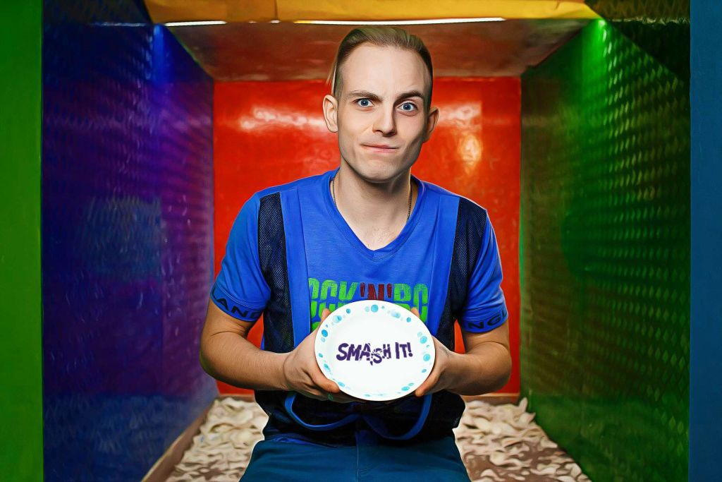 파란색 셔츠를 입은 사람이 하얀색 접시에 "SMASH IT!" 라고 쓰여 있고, 화려한 방에 서 있습니다.