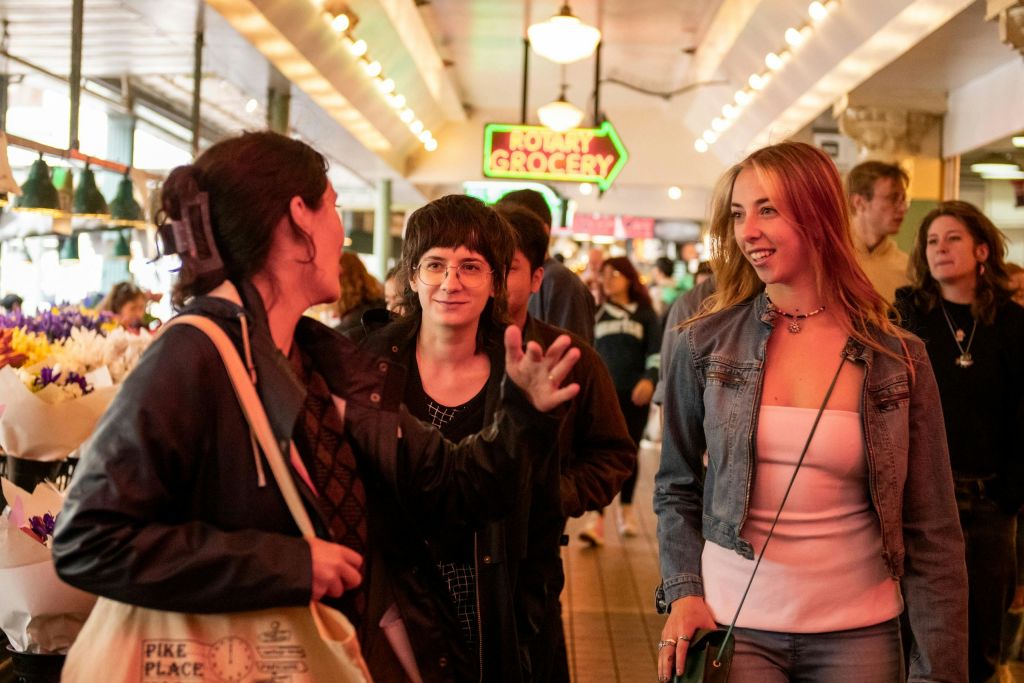 밝게 빛나는 실내 시장을 거닐고 있는 사람들. 배경에 '식료품' 이라고 적힌 네온 사인이 보입니다.