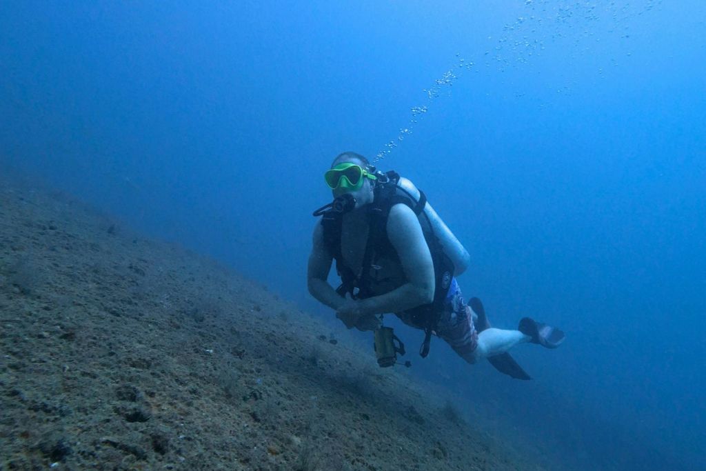 탱크와 마스크를 착용한 수중 스쿠버 다이버가 기포가 솟아오르는 바다 바닥 근처에서 수영하고 있습니다.