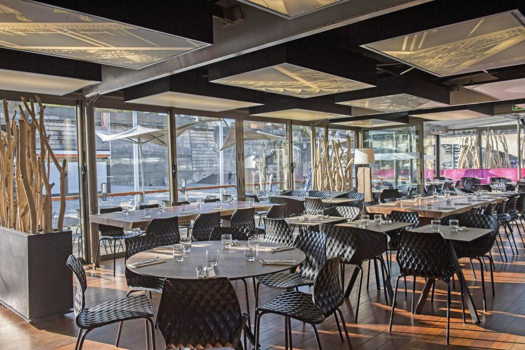 유리잔과 식기류가 놓인 빈 테이블이 있는 현대적인 레스토랑 내부에는 커다란 창문과 검은색 의자가 있습니다.