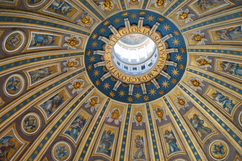 중앙 개구부를 둘러싼 금색 장식, 파란색 액센트, 라틴 문양이 돋보이는 화려한 돔 천장.