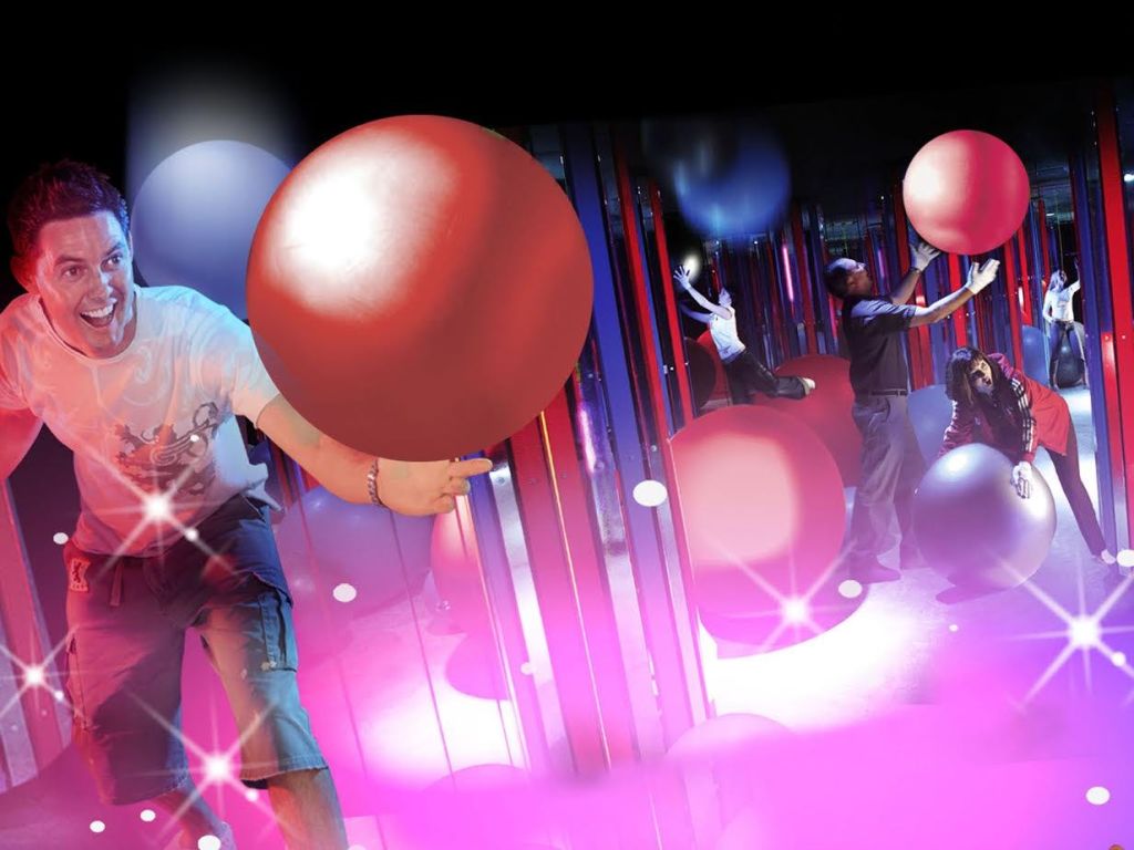 거울과 반사가 있는 화려하고 빛나는 방에서 크고 빨간 팽창식 공을 들고 웃는 사람.