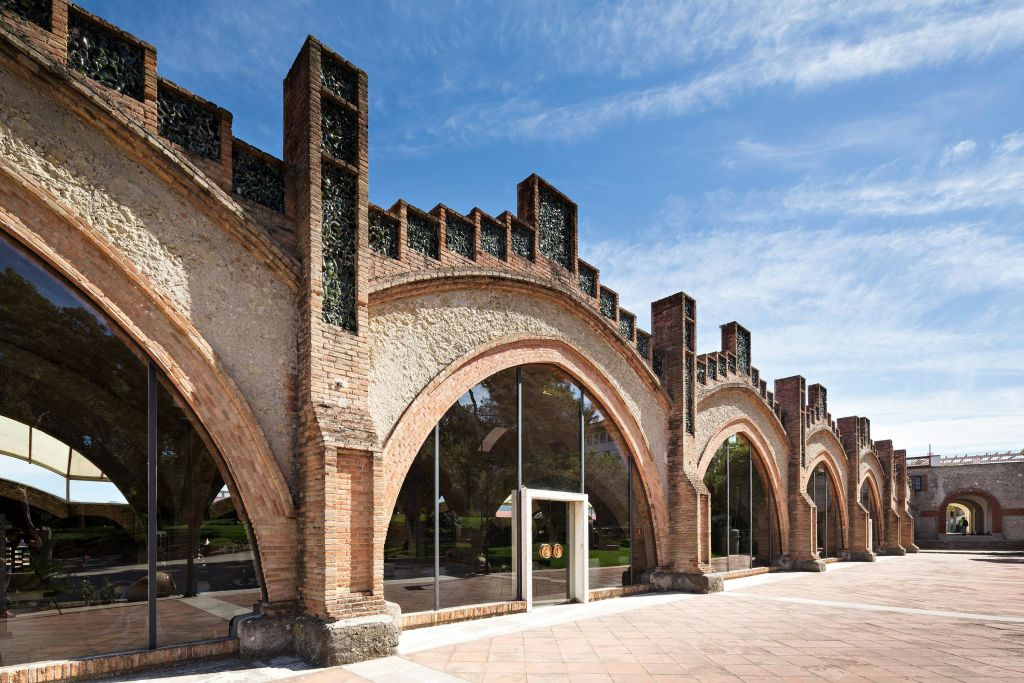 파란 하늘 아래 장식 요소가 특징인 벽돌 아치와 커다란 유리창이 있는 건물입니다.