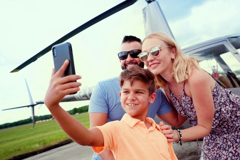 화창한 날 헬리콥터 앞에서 한 남녀와 어린이가 셀카를 찍고 있습니다.