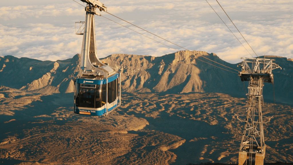 '텔레페리코 델 테이데 (Teleférico del Teide)' 라는 이름의 파란색 케이블카가 흐린 하늘 아래 험준한 산 풍경 위에 매달려 있습니다.