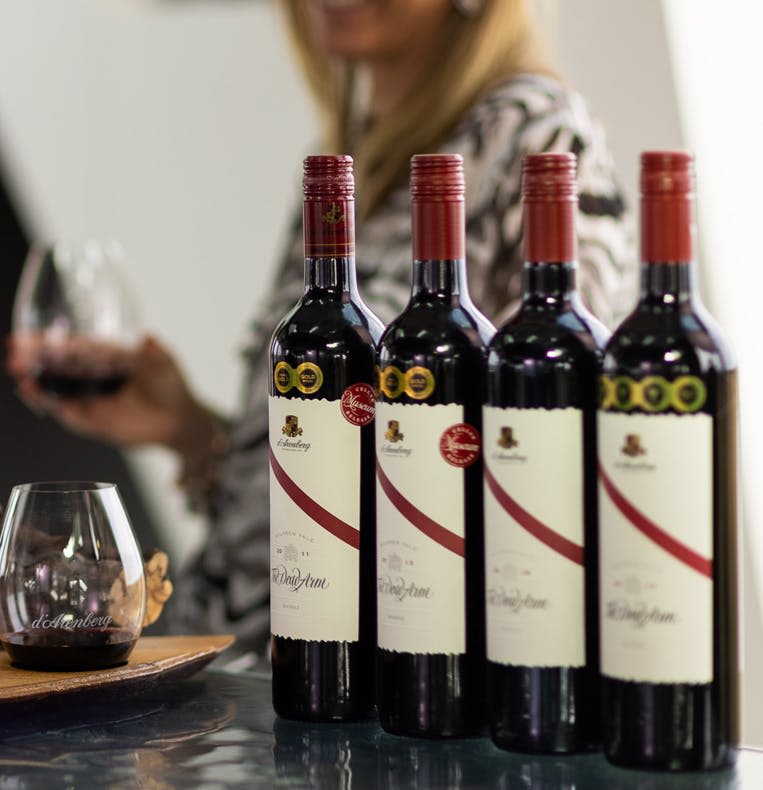 한 사람이 와인잔을 배경으로 카운터에 놓인 레드 와인 4병.