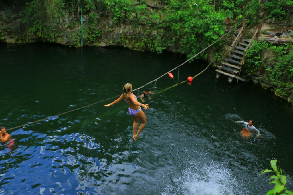 푸르름과 나무 계단을 배경으로 자연스러운 물구멍으로 뛰어드는 수영복을 입은 사람.