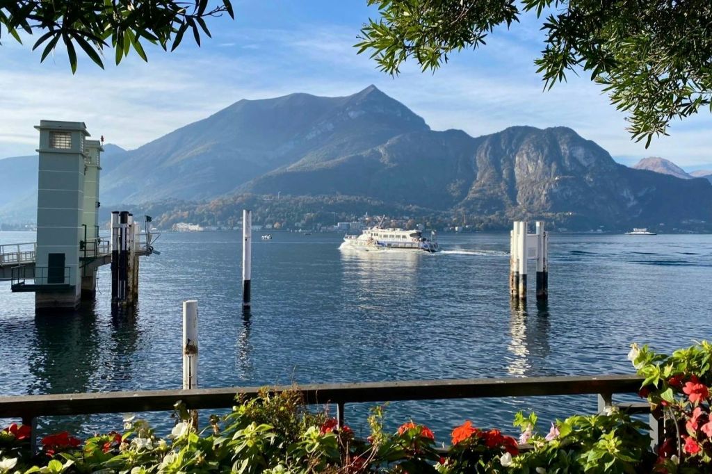 보트가 산으로 둘러싸인 호수를 가로질러 이동합니다. 화려한 꽃과 녹음이 전경을 장식합니다.