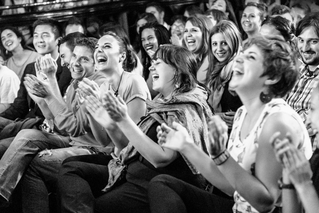 가까이 앉아 미소를 짓고 박수를 치며 공연이나 이벤트를 즐기는 것처럼 보이는 사람들입니다. 흑백 이미지.