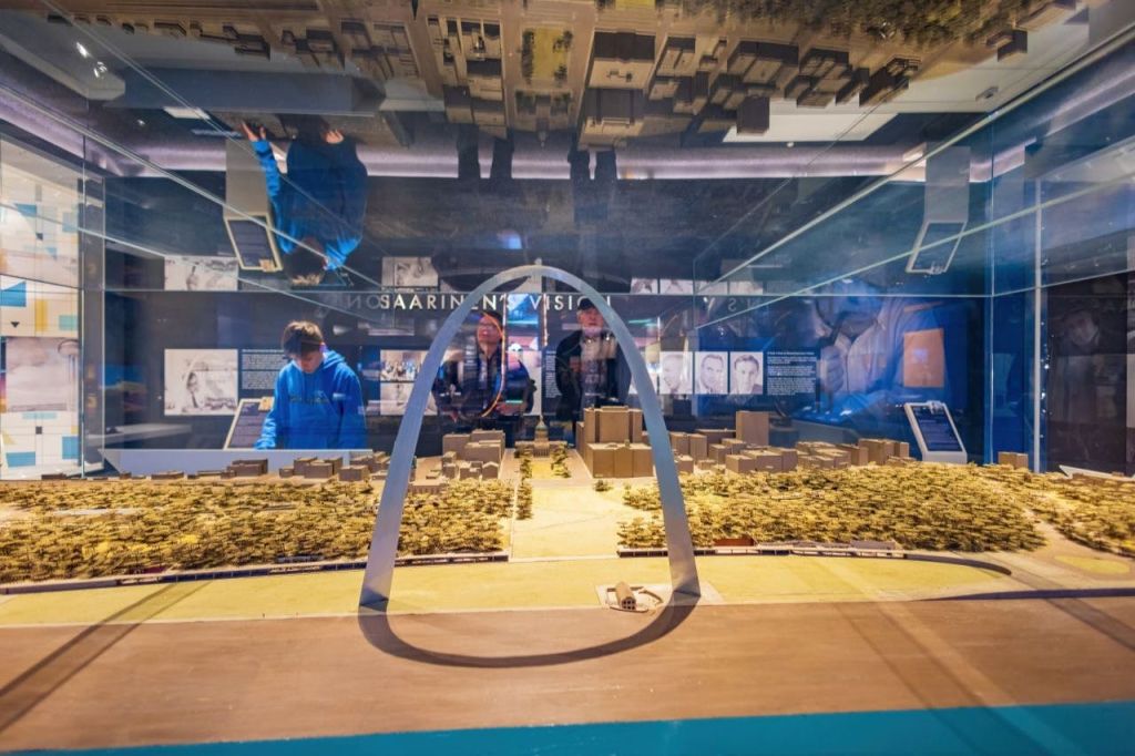 박물관 전시관에서 게이트웨이 아치가 있는 도시 풍경의 스케일 모델을 관찰하는 방문객.