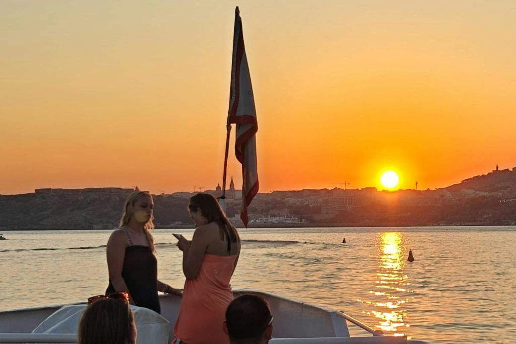 해가 질 무렵 보트를 타고 있는 두 명의 여성이 깃발을 들고 물과 먼 해안선을 배경으로 아름다운 풍경을 감상하고 있습니다.