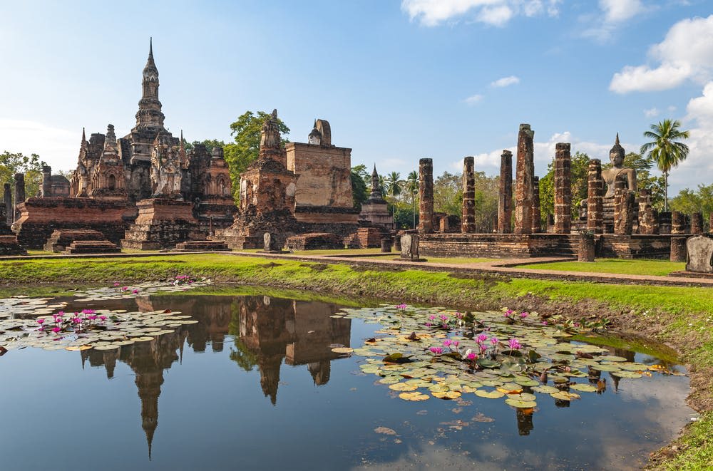 맑고 푸른 하늘 아래, 백합 패드로 덮인 연못 옆에 석조 건축물과 기둥이 있는 고대 유적지.