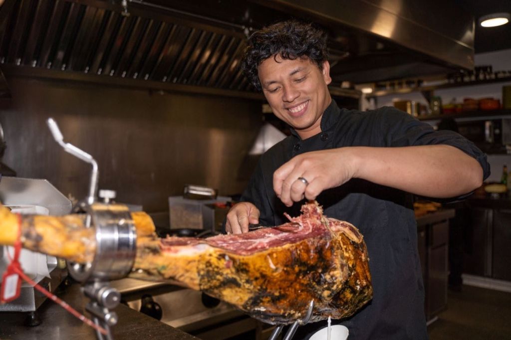 주방장이 상업용 주방에서 잘게 썬 고기를 썰며 미소를 짓고 있습니다.