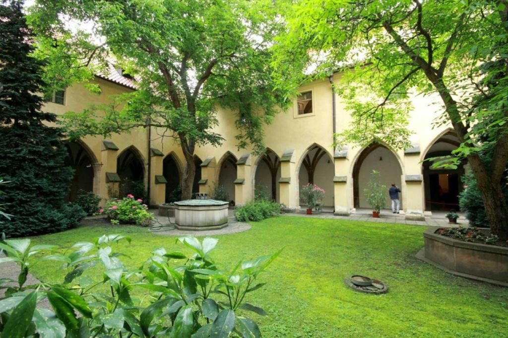 중앙 분수대, 울창한 녹음, 아치형 출입구, 복도를 걷는 사람이 있는 평화로운 마당입니다.