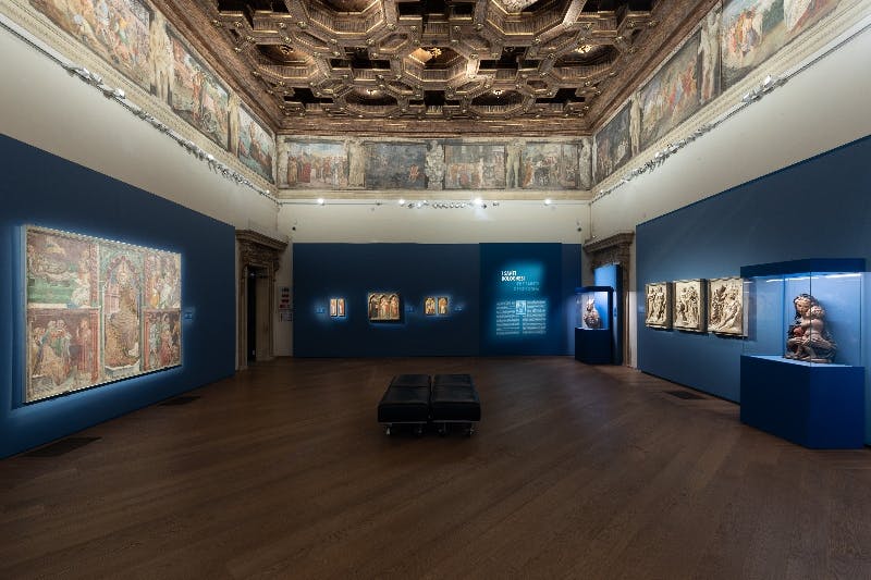 나무 바닥, 장식된 천장, 벽 프레스코화, 흰색 벽에 검은색 추상 조각이 있는 미술관입니다.